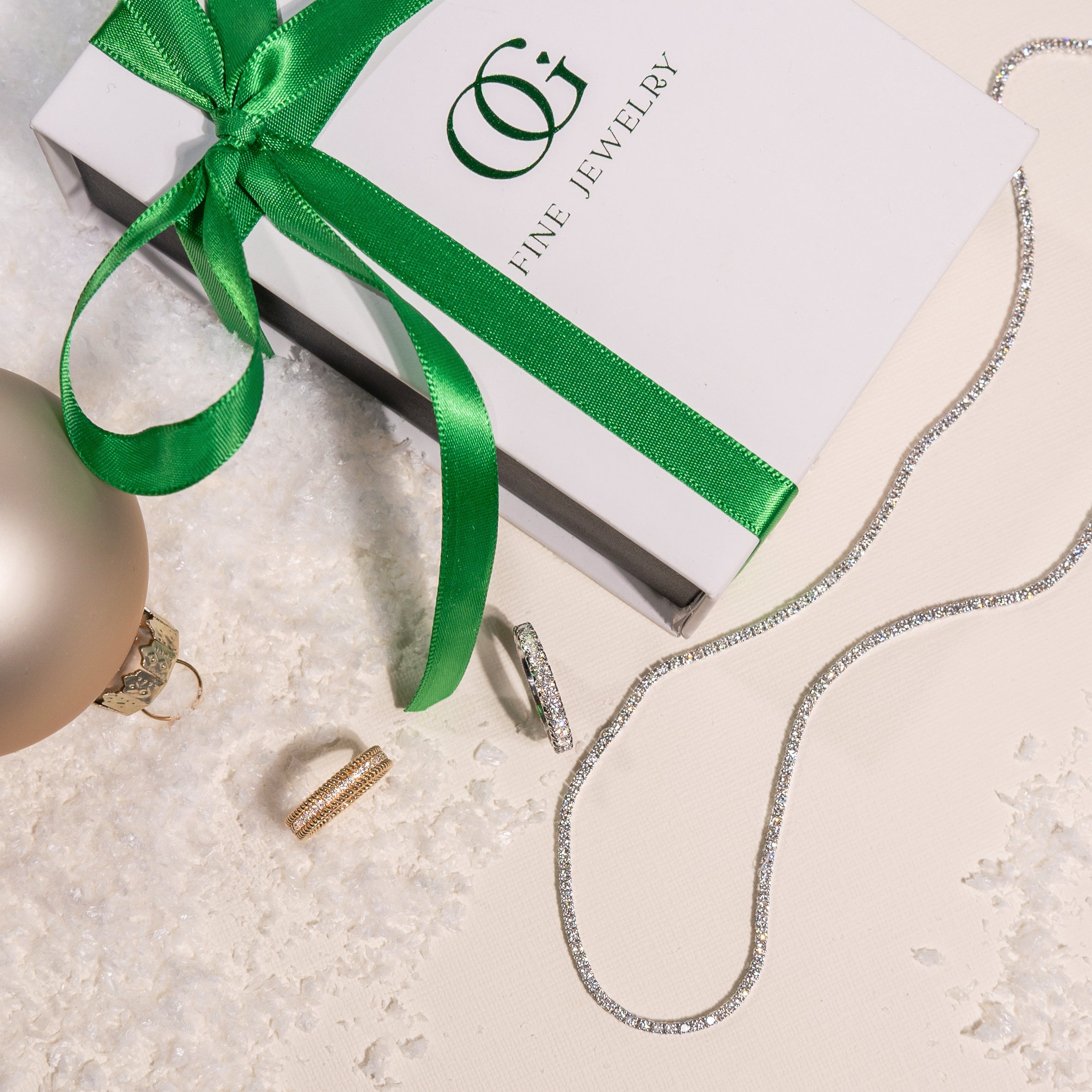 Jewelry set with a necklace, ring, and earrings on a white surface with a green ribbon and 'OG Fine Jewelry' box.